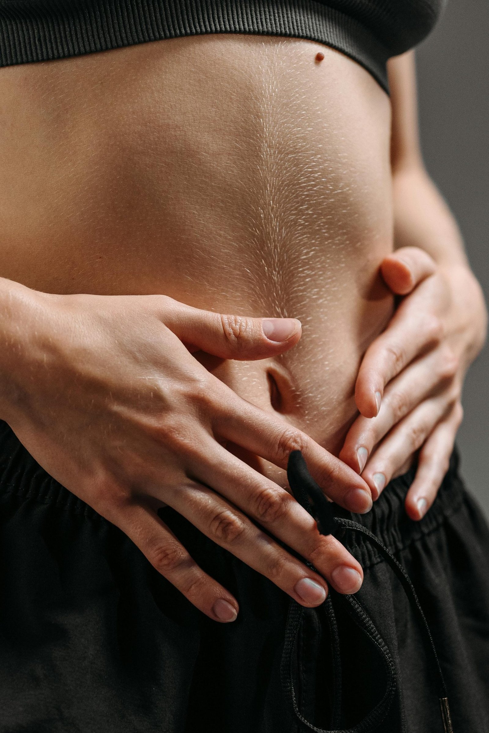Programs Hands resting on a toned stomach in sportswear, reflecting fitness and health.